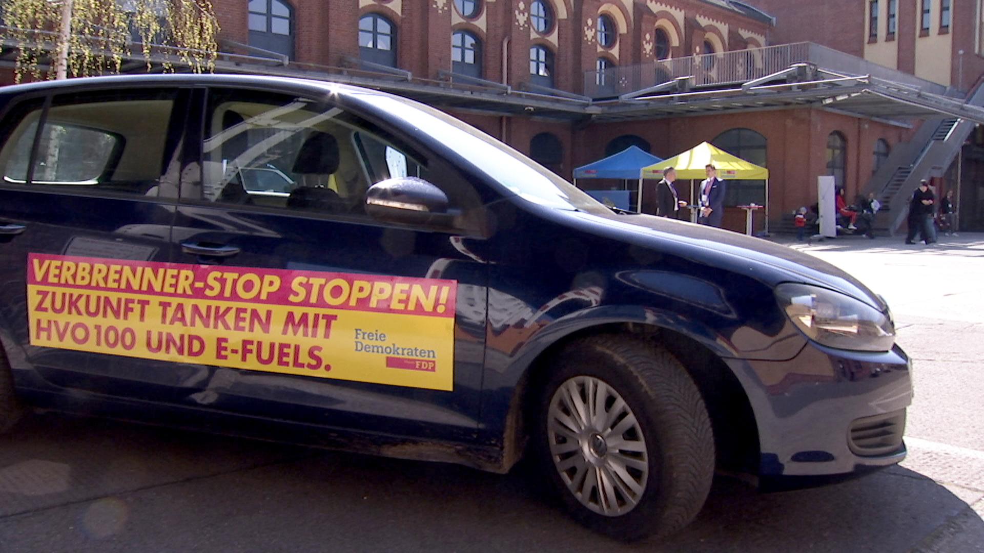 Blaue VW-Pkw mit FDP-Werbebanner auf Türen "Verbrenner-Stop stoppen! - Zukunft tanken mit HVO 100 und E-Fuels"