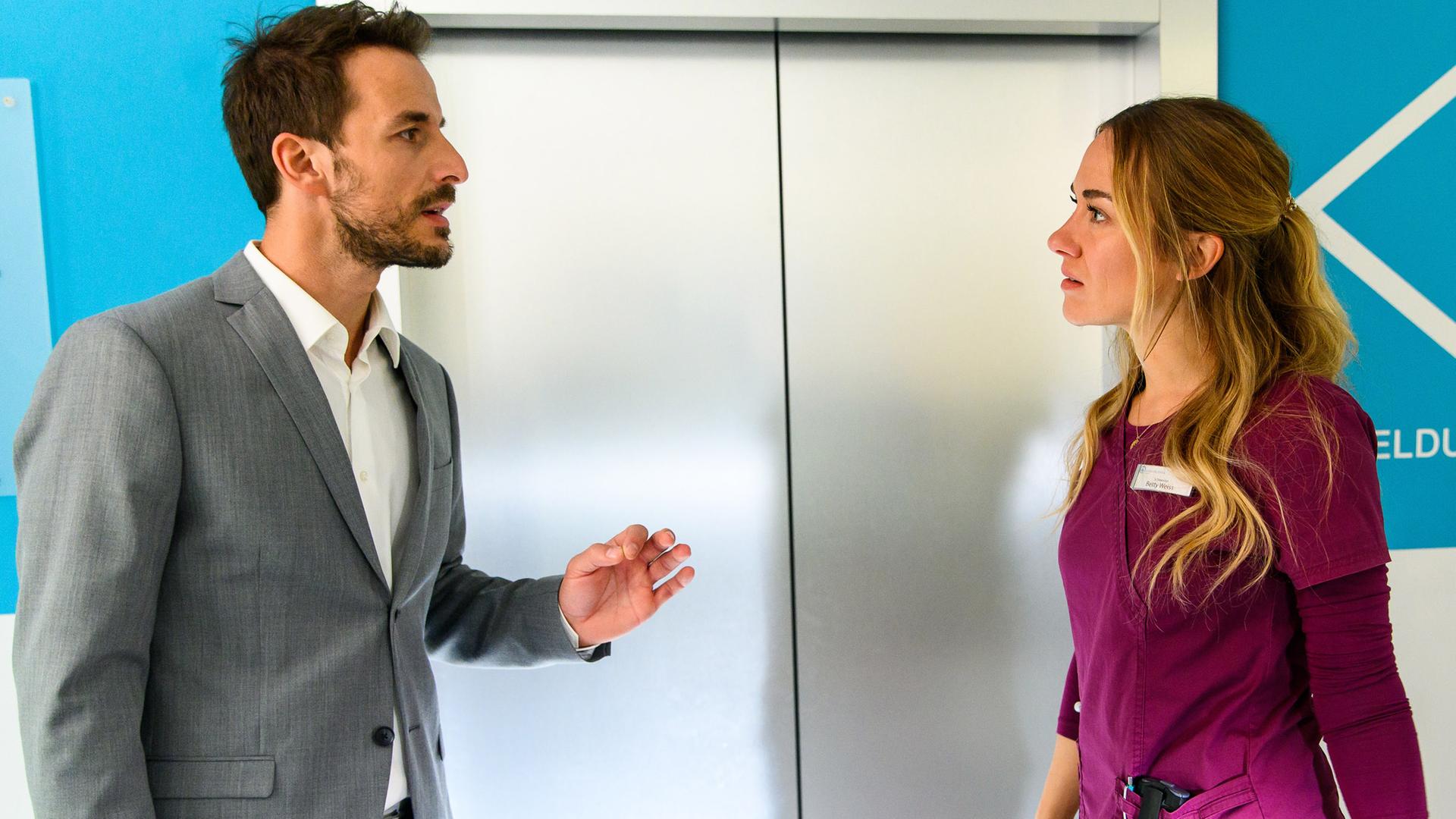 Dr. Frank Stern (Max Alberti) und Betty Weiss (Annina Hellenthal) stehen diskutierend vor dem Krankenhausfahrstuhl.