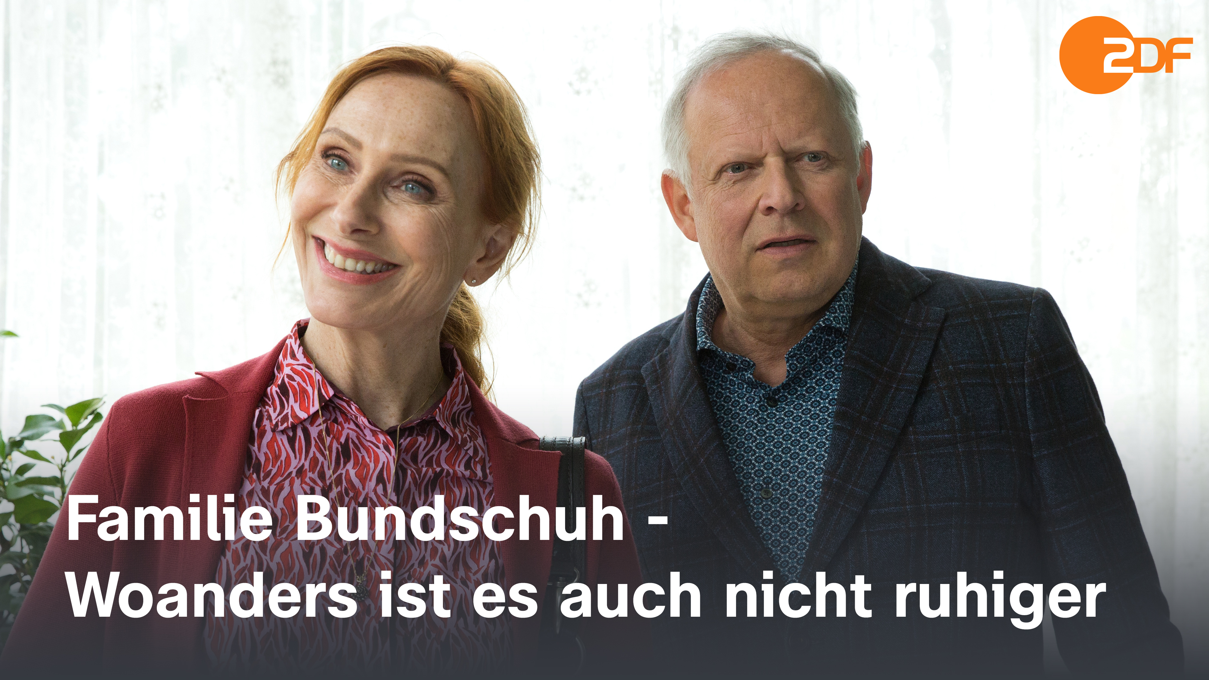 Gundula (Andrea Sawatzki) und Gerald (Axel Milberg) stehen in einem Zimmer vor einem Fenster. Gundula hat ein überfreundliches Lächeln auf dem Gesicht, Gerald blickt zuversichtlich.