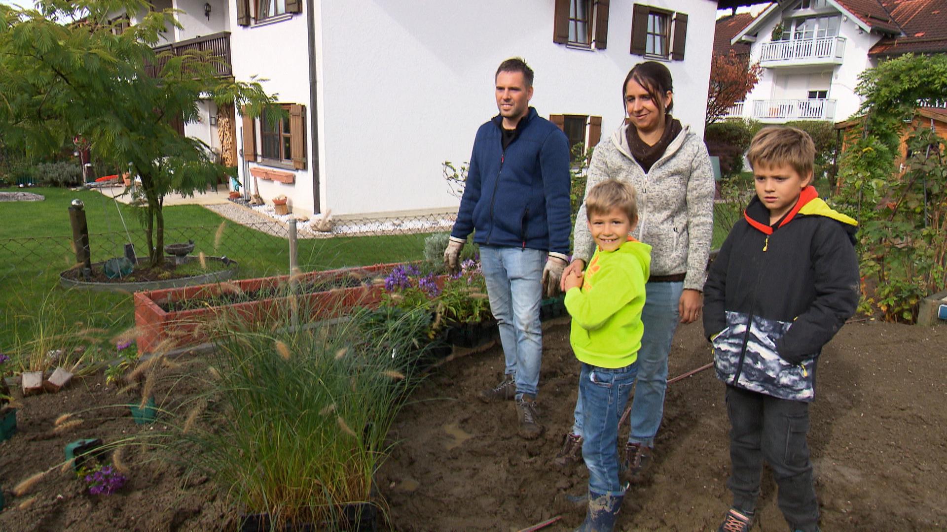 Familie Schwinghammer, bestehend aus Vater, Mutter und zwei Söhnen, auf einem Gartengrundstück mit Haus im Hintergrund.