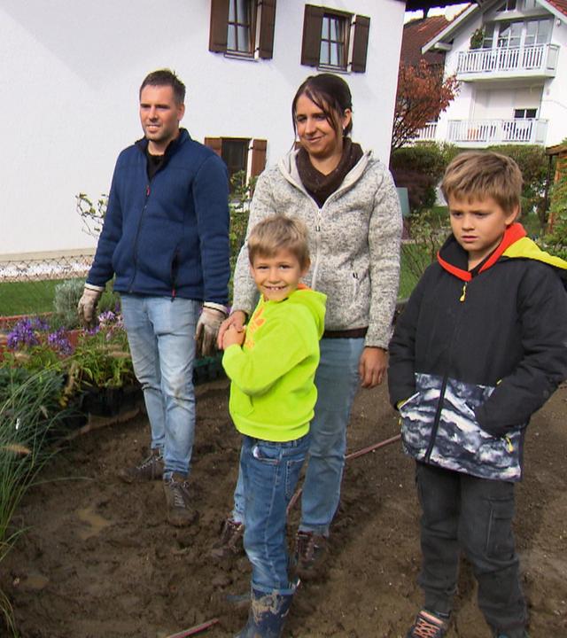 Familie Schwinghammer, bestehend aus Vater, Mutter und zwei Söhnen, auf einem Gartengrundstück mit Haus im Hintergrund.