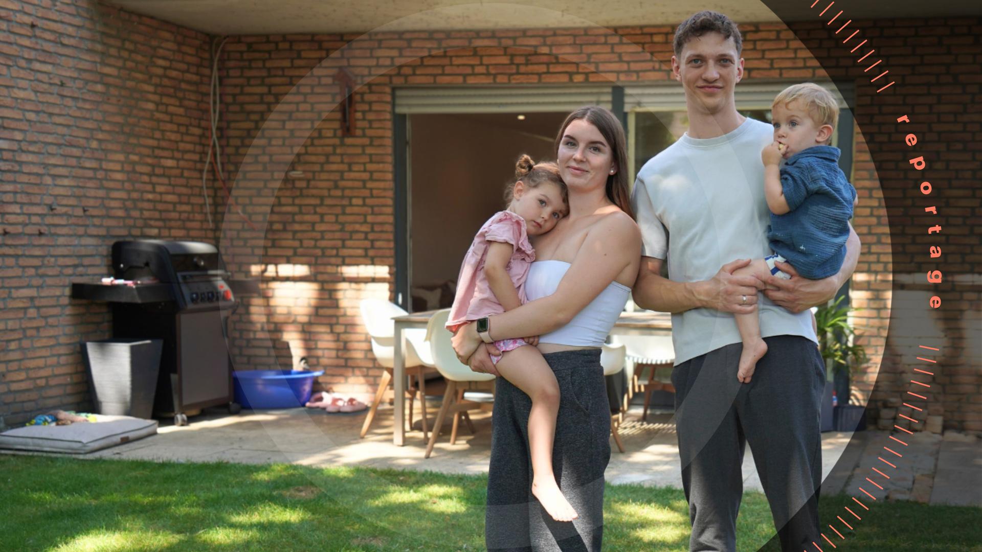 Katharina und Jannik S. stehen im Garten vor einem Haus. Sie haben ihre beiden Kinder auf dem Arm.