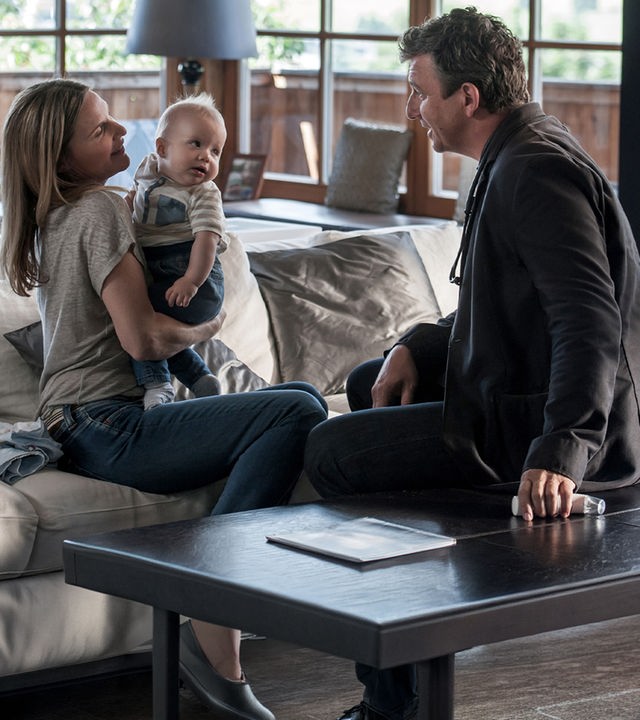 "Der Bergdoktor - Familienfieber (1)": Sabine Wimmer (Nele Mueller-Stöfen) sitzt auf der Couch und hält ihren Sohn Leo auf dem Arm. Vor ihr sitzt Dr. Martin Gruber (Hans Sigl) und betrachtet das Kind.
