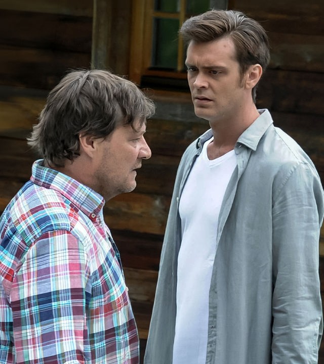 "Der Bergdoktor - Familienfieber (2)": Jakob Wimmer (Harald Windisch) und Tobias Ritter (Sebastian Fräsdorf) stehen sich mit ernstem Gesicht vor einem Holzhaus gegenüber.