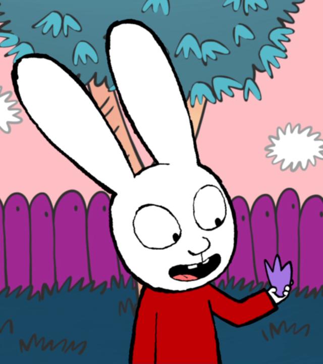 Simon hält in seiner linken Hand ein lila Blume. Rechts von ihm ist ein rosafarbener Busch mit diesen Blüten zu sehen, im Hintergrund ein lila Zaun und ein grüner Baum. 