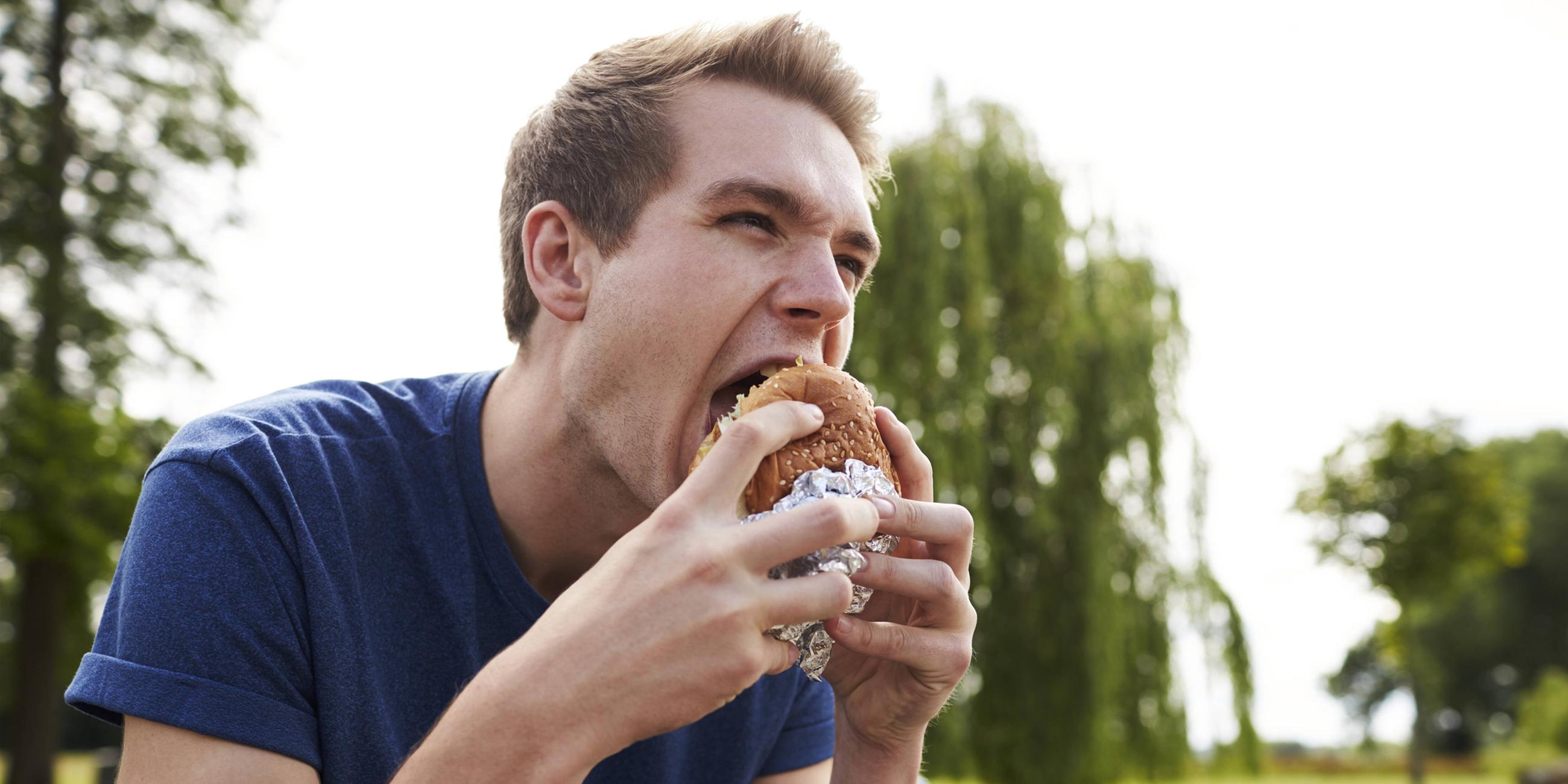 Ein junger Mann isst eine Hamburger in einem Park
