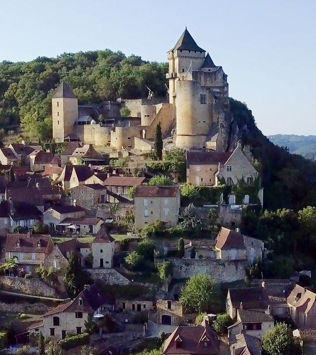 Mittelalterliche Burg Castelnaud an einem Flussufer oberhalb eines Dorfes. Im Hintergrund zwei Heißluftballons und eine weitere Burganlage.