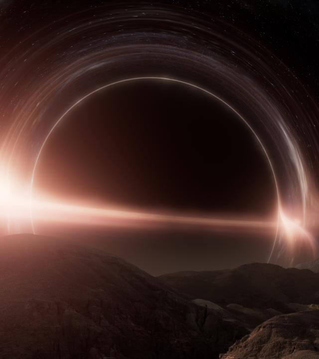 Computeranimation eines Schwarzen Lochs, das von leuchtenden Ringen umgeben ist. Im Vordergrund die felsige Oberfläche eines Planeten.