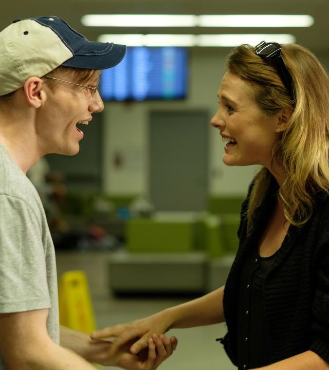 "Fatale Zusammentreffen: Die Hoffnung stirbt zuletzt": Nachgestellte Szene: Ein Mann und eine Frau an einem Flughafen-Terminal begrüßen sich erfreut.