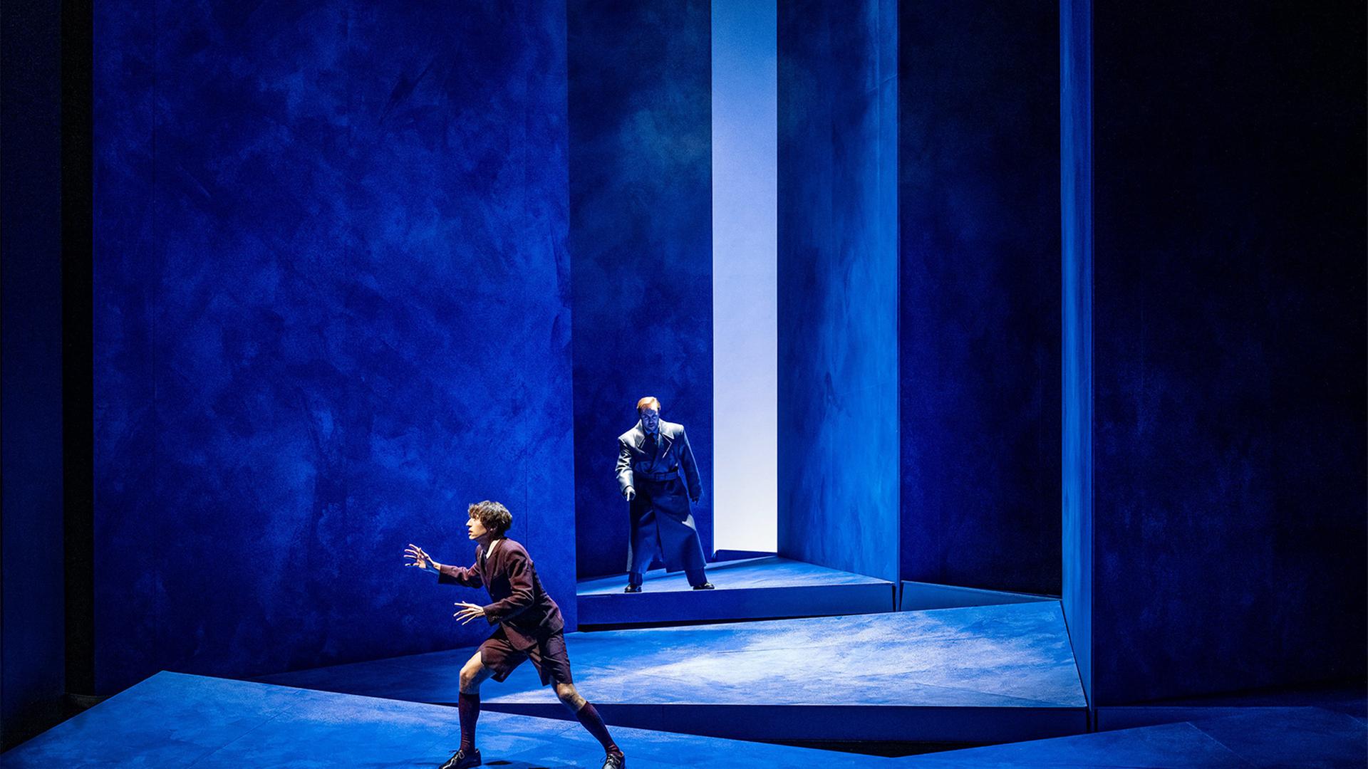 Auf einer blauen Bühne stehen zwei Männer hintereinander.