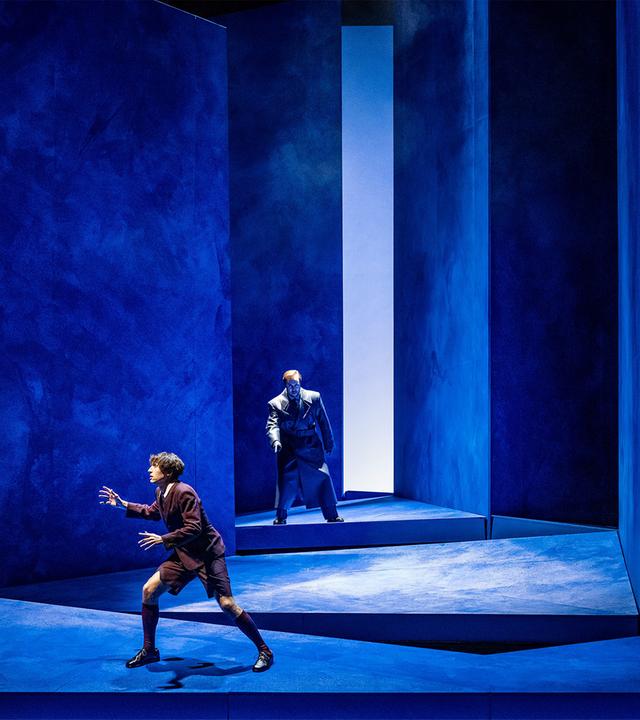 Auf einer blauen Bühne stehen zwei Männer hintereinander.