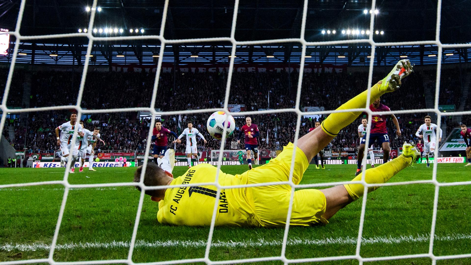 Augsburgs Torwart Finn Dahmen (M) hält den Elfmeter von Leipzigs Lois Openda (3.v.r). 