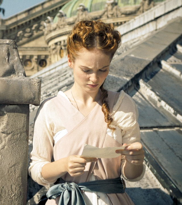 Thea steht auf dem Dach der Pariser Oper. Sie liest einen Brief, den sie in den Händen hält.