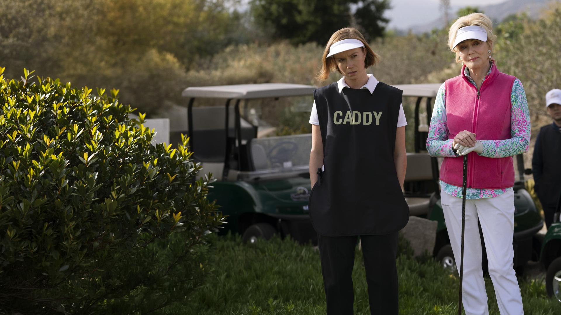 "Hacks - Fehlschläge": Deborah (Jean Smart) und Ava (Hannah Einbinder) stehen in Golfoutfits vor Golfcarts. Deborah hält einen Golfschläger in ihren Händen. Ava schaut skeptisch und hat ihre Hände in den Hosentaschen. Im Hintergrund steht eine weitere Person (Komparse) zwischen Golfcarts.