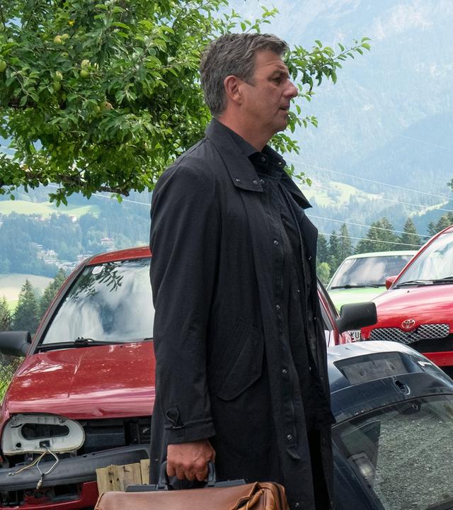 Vor einer Werkstatt stehen sich Martin (Hans Sigl) und Holger Brandstetter (Florian Panzner) gegenüber. Im Hintergrund stehen viele reparaturbedürftige Autos.