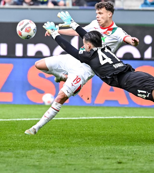 Augsburgs defensiver Mittelfeldspieler Robin Fellhauer versucht auf das Tor zu schießen, Heidenheims Torwart Diant Ramaj hechtet in Richtung Ball