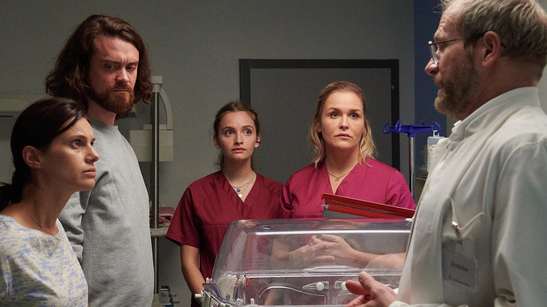 Dr. Keller (Thomas Limpinsel, r.) teilt den entsetzten Eltern Nadia (Leni Adams, l.) und Felix Berger (Sebastian Fräsdorf, 2.v.l.) mit, dass ihr Baby umgehend operiert werden muss. Auch Hebamme Lena Lorenz (Judith Hoersch, 2.v.r.) und Praktikantin Celine Gollert (Paulina Rümmelein, M.) sind schockiert über die schlechte Nachricht.