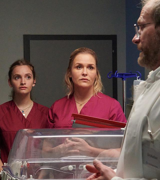 Dr. Keller (Thomas Limpinsel, r.) teilt den entsetzten Eltern Nadia (Leni Adams, l.) und Felix Berger (Sebastian Fräsdorf, 2.v.l.) mit, dass ihr Baby umgehend operiert werden muss. Auch Hebamme Lena Lorenz (Judith Hoersch, 2.v.r.) und Praktikantin Celine Gollert (Paulina Rümmelein, M.) sind schockiert über die schlechte Nachricht.