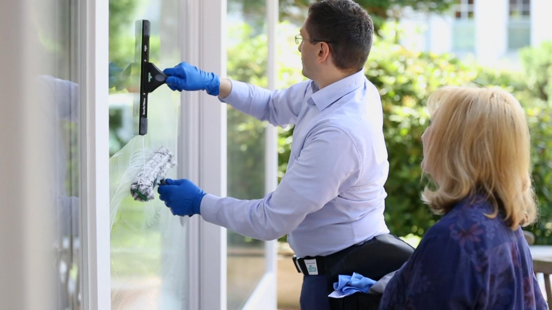 Mann putzt Fenster, Frau schaut zu