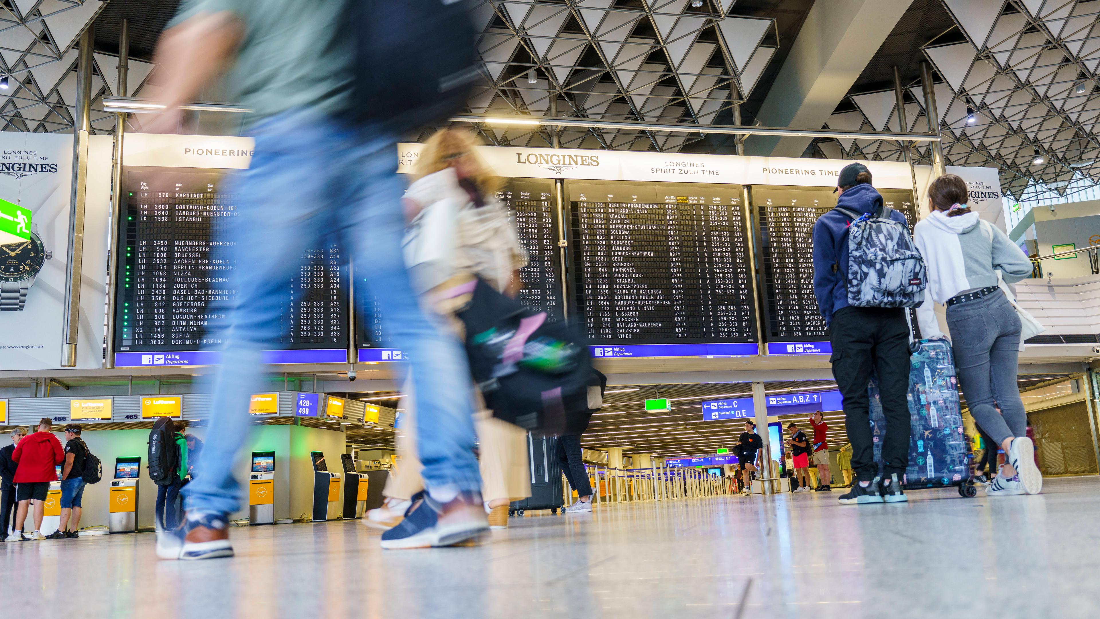  Reisende gehen im Flughafen Frankfurt Main an der Anzeigetafel vorbei. In 4 Tagen beginnen in Hessen die Sommerferien