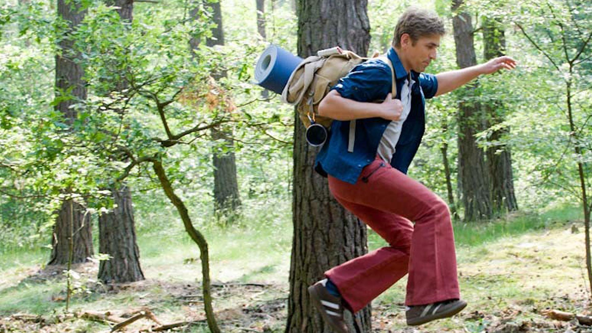 Fritz Fuchs mit Rucksack im Wald unterwegs. Er springt über ein kleines Hindernis.