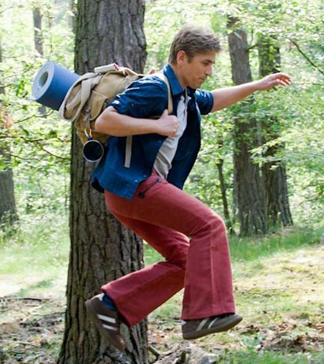 Fritz Fuchs mit Rucksack im Wald unterwegs. Er springt über ein kleines Hindernis.