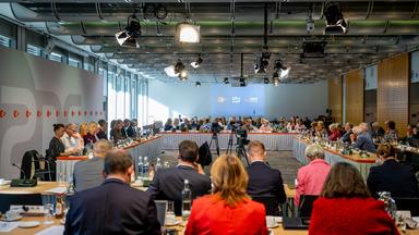 Blick in einen großen Konferenzraum während einer Sitzung des ZDF-Fernsehrats. Zahlreiche Menschen sitzen an hufeisenförmig angeordneten Tischen; im Vordergrund sind einige von hinten zu sehen. In der Mitte des Raums stehen Kameras auf Stativen