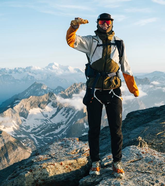 Ein Mann in Trekking Kleidung steht auf einem Berggipfel.