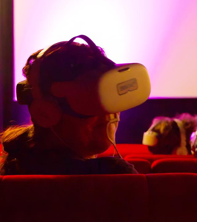 In einem Kinosaal sieht man Personen, die Kopfhörer und VR-Brillen tragen.