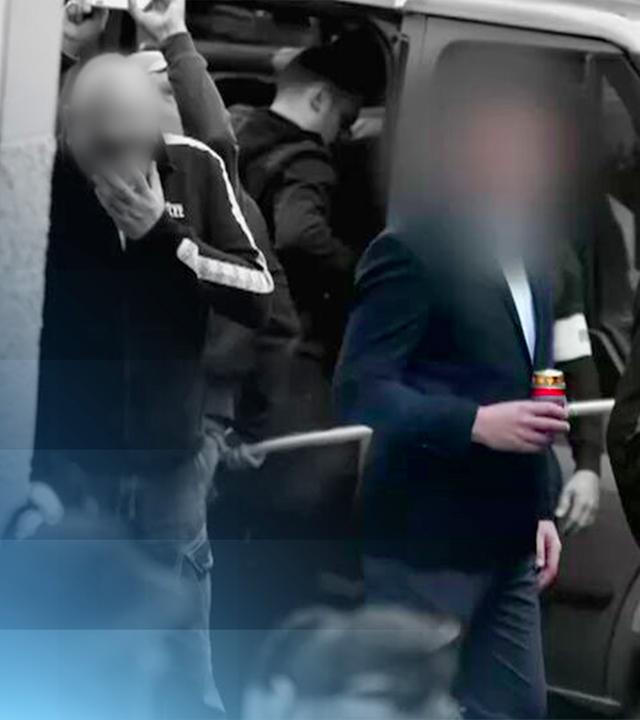 Mehrere dunkel gekleidete Männer stehen vor einem Auto