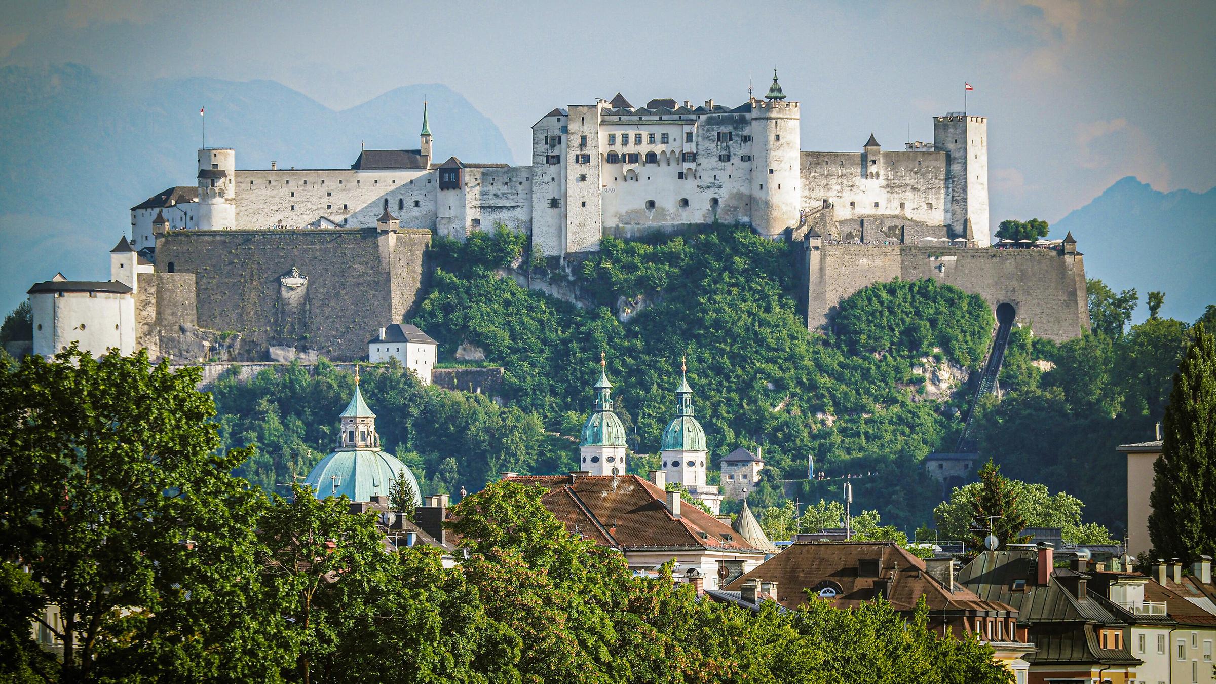 Burg auf einem Berg vor den Alpen.