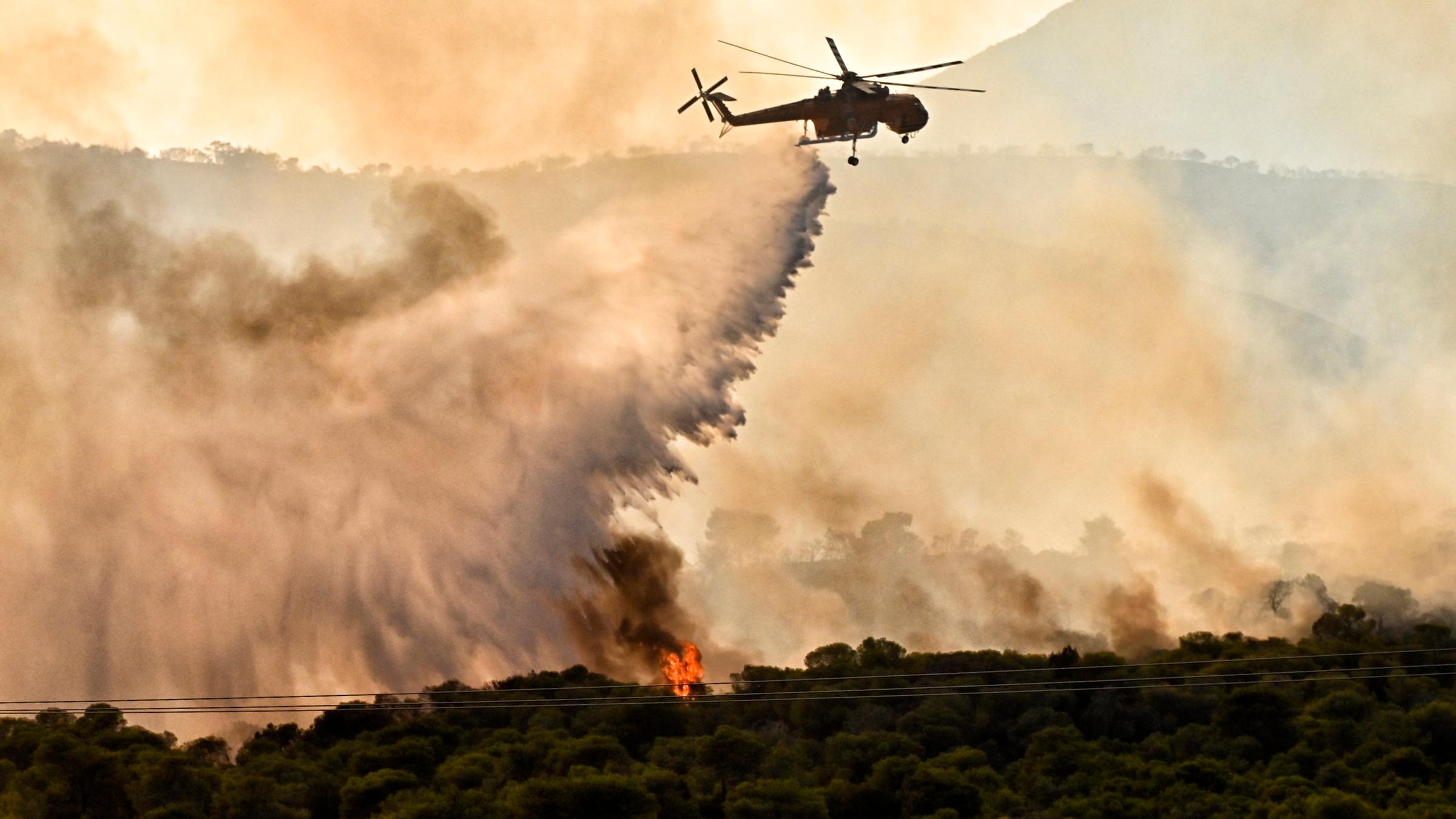 Ein Löschhelikopter wirft Wasser über einem Waldbrand ab.