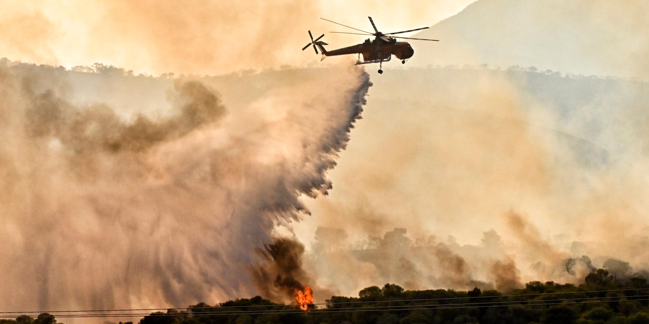 Ein Löschhelikopter wirft Wasser über einem Waldbrand ab.