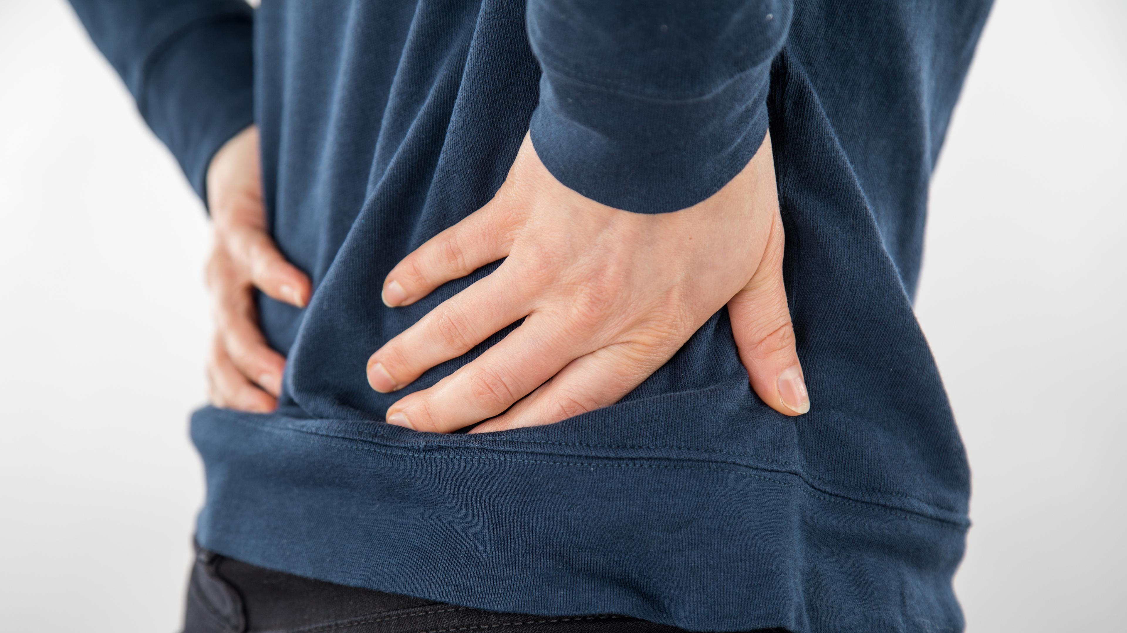 Eine Person leidet an Rückenschmerzen und hält sich die Hände an den unteren Rücken.