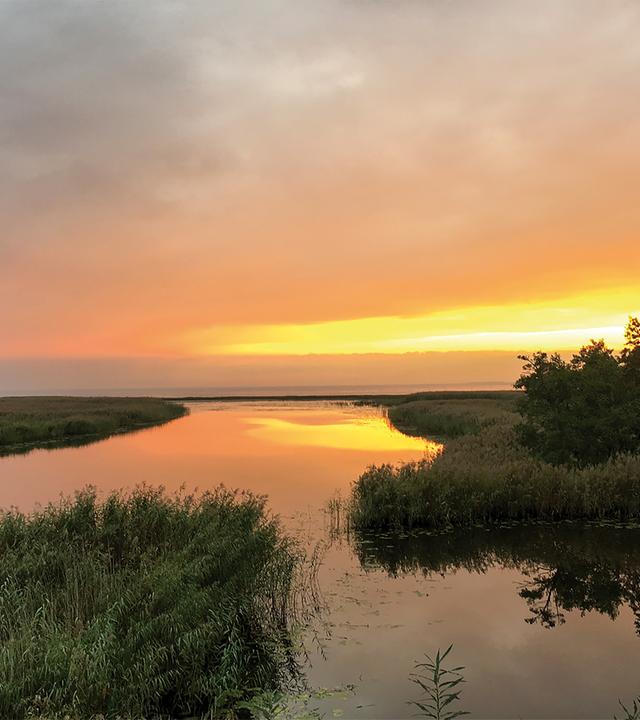 Man sieht eine Flusslandschaft bei Sonnenuntergang.