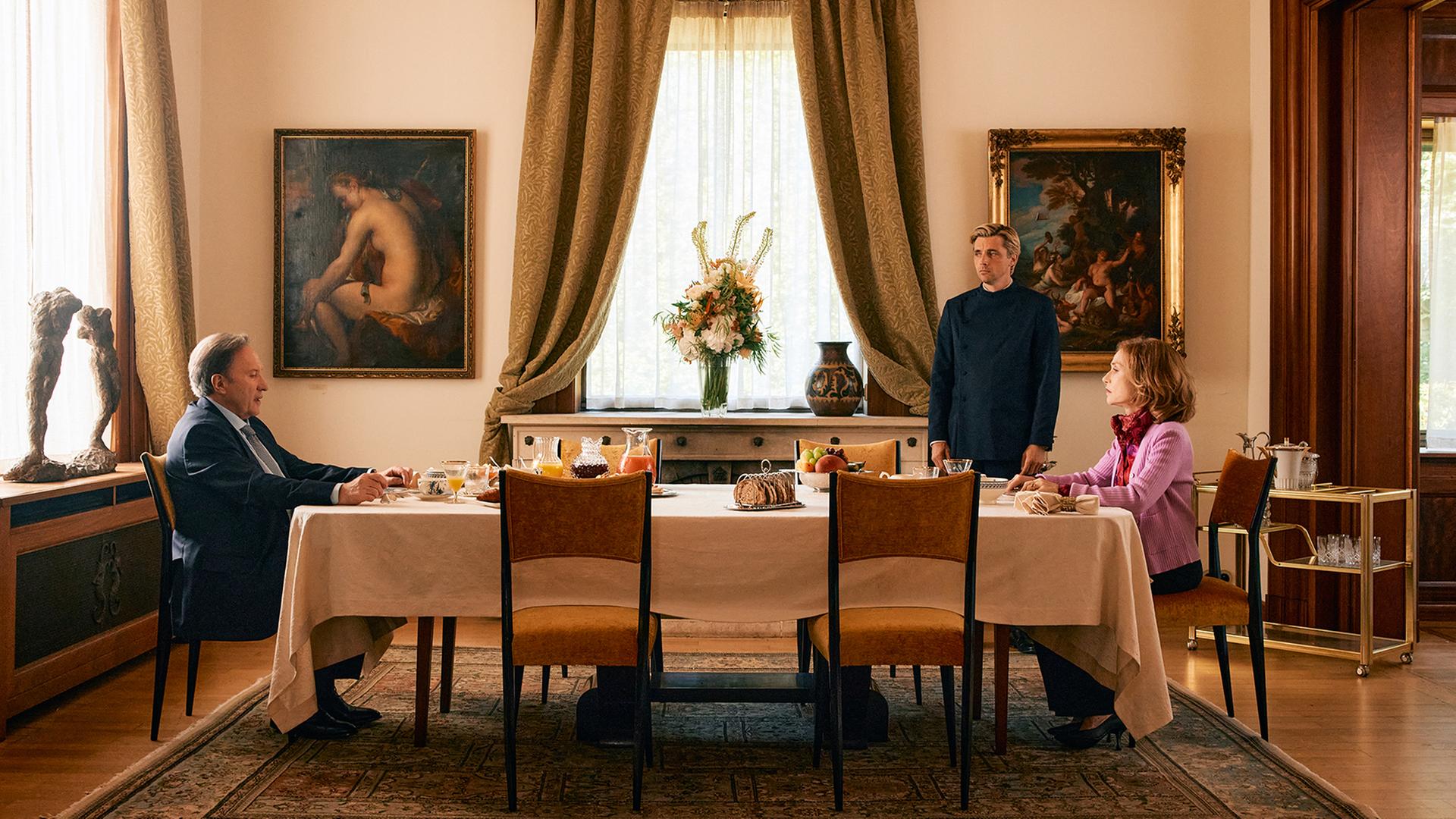 Man sieht eine Tafel an der ein Mann und eine Frau sitzen. Ein Butler steht neben dem Tisch.