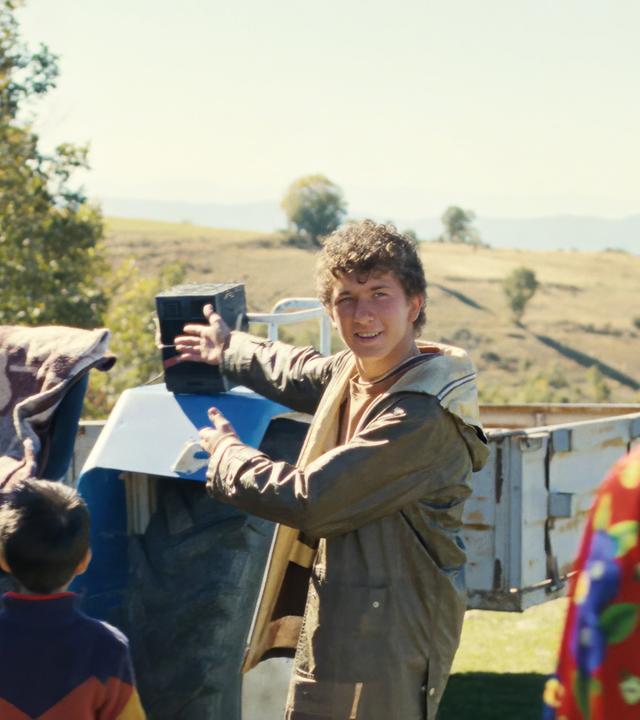 Ein junger Mann steht vor einem Traktor. Neben ihm steht eine Person in Tracht.
