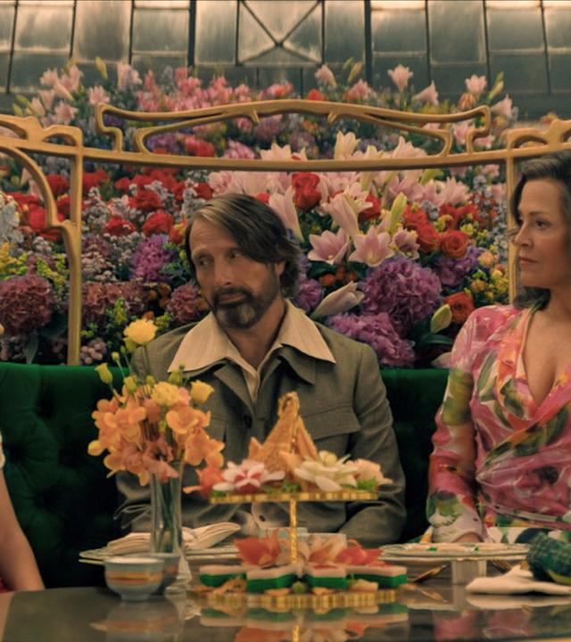 Ein Mädchen, ein Mann und eine Frau sitzen an einer im Art-Nouveau-Stil geschmückten Kaffee-Tafel.