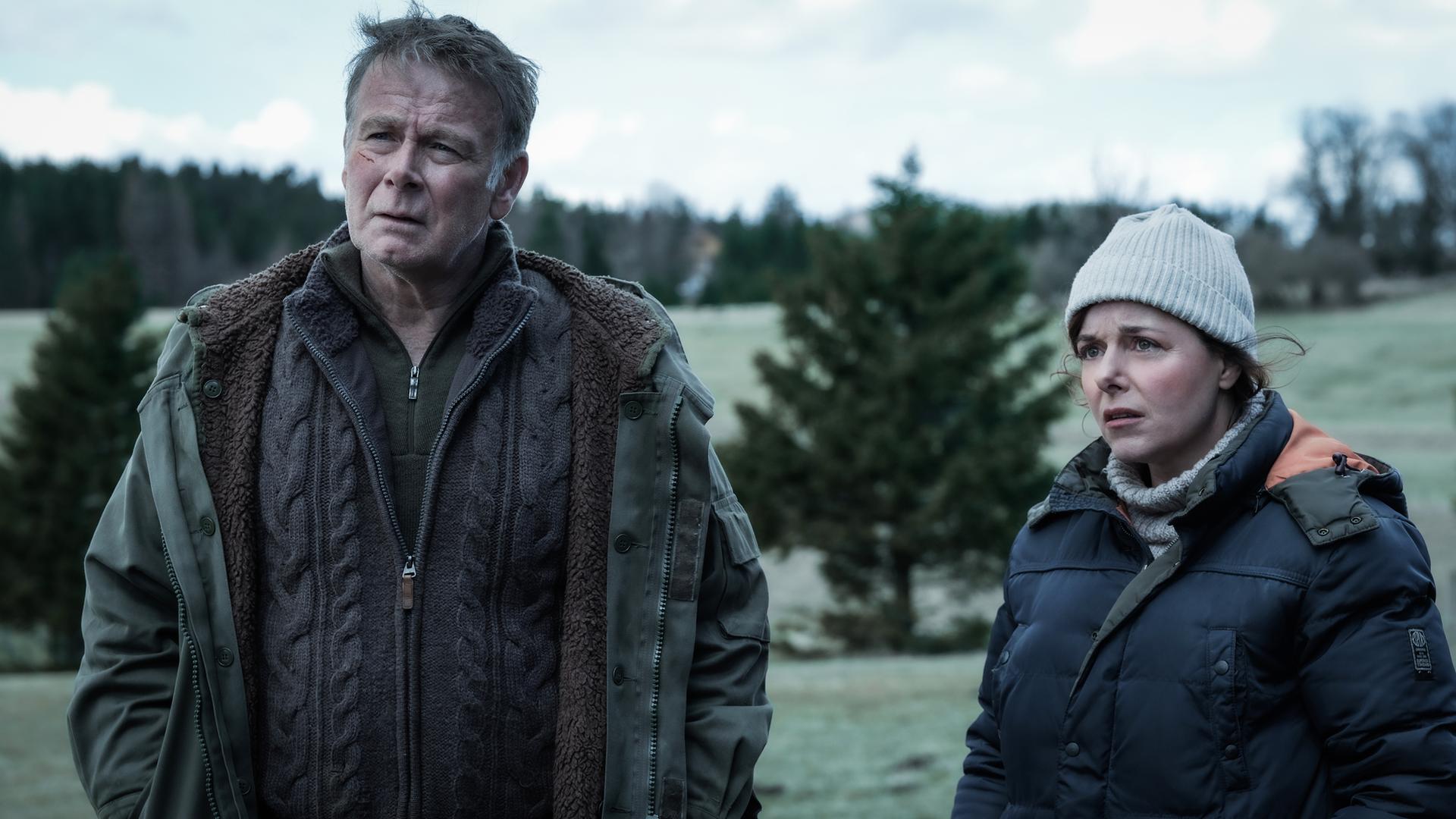 Ein Mann und eine Frau stehen in winterlicher Kleidung vor einem Waldstück.