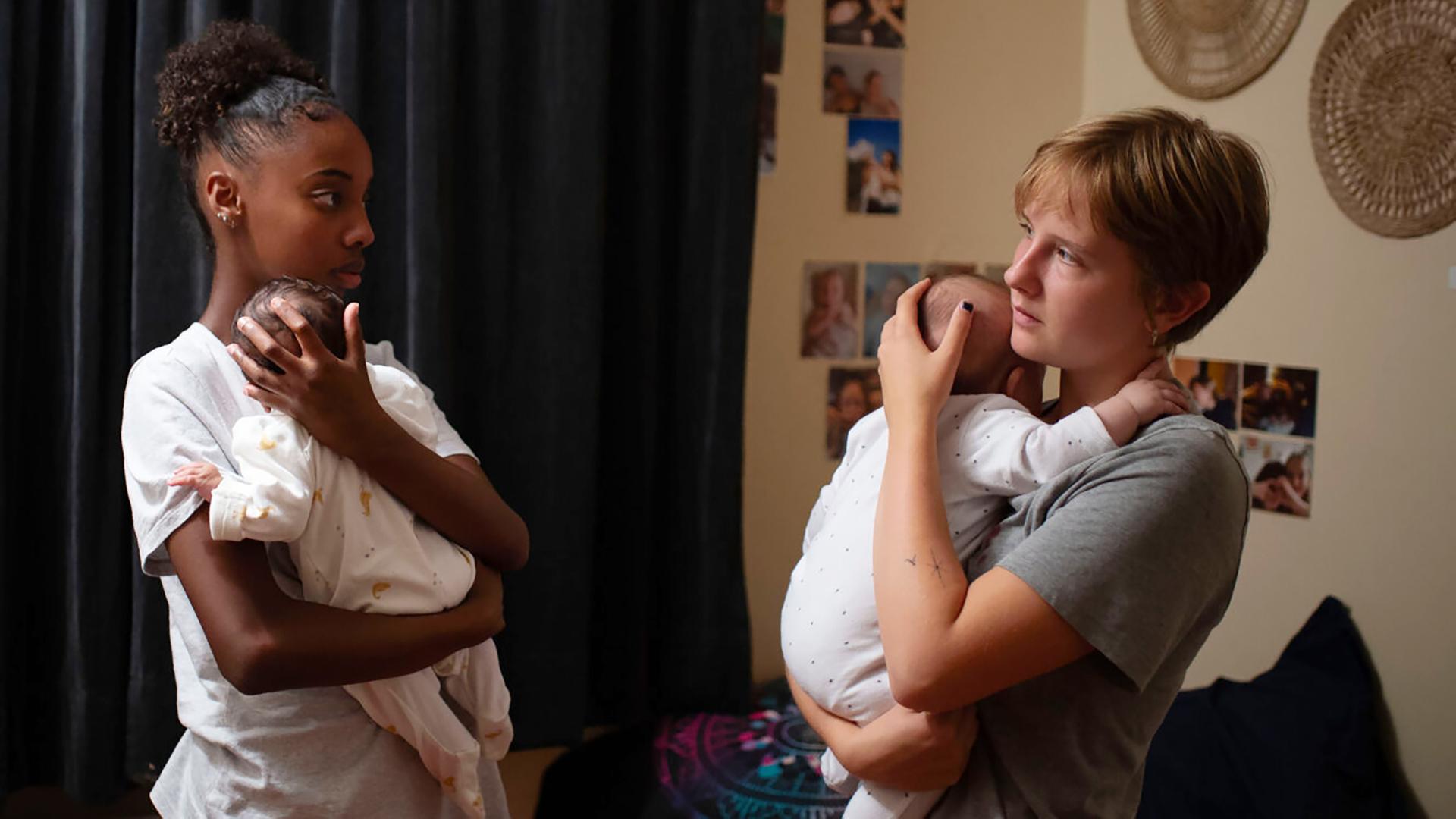 Zwei junge Frauen stehen sich gegenüber und halten ihre Babies auf dem Arm.
