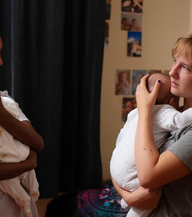 Zwei junge Frauen stehen sich gegenüber und halten ihre Babies auf dem Arm.