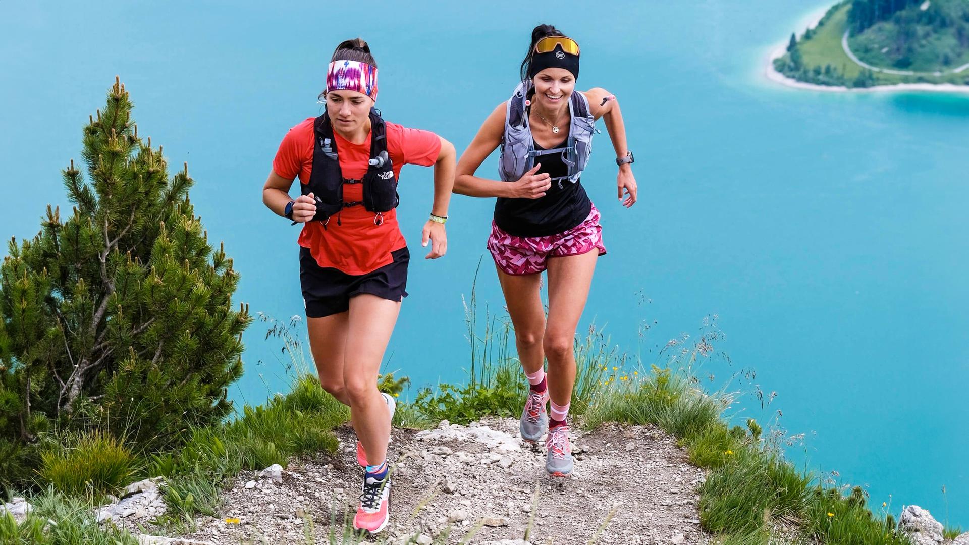 Zwei Frauen in Sportbekleidung laufen auf einem Bergweg.