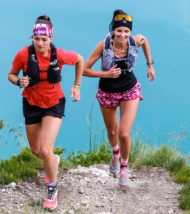 Zwei Frauen in Sportbekleidung laufen auf einem Bergweg.