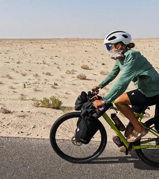 Eine Frau fährt mit dem Fahrrad durch die Wüste.