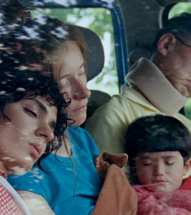 Auf der Rückbank eines Autos sitzen ein Mann, zwei Frauen und ein Kind und schlafen.