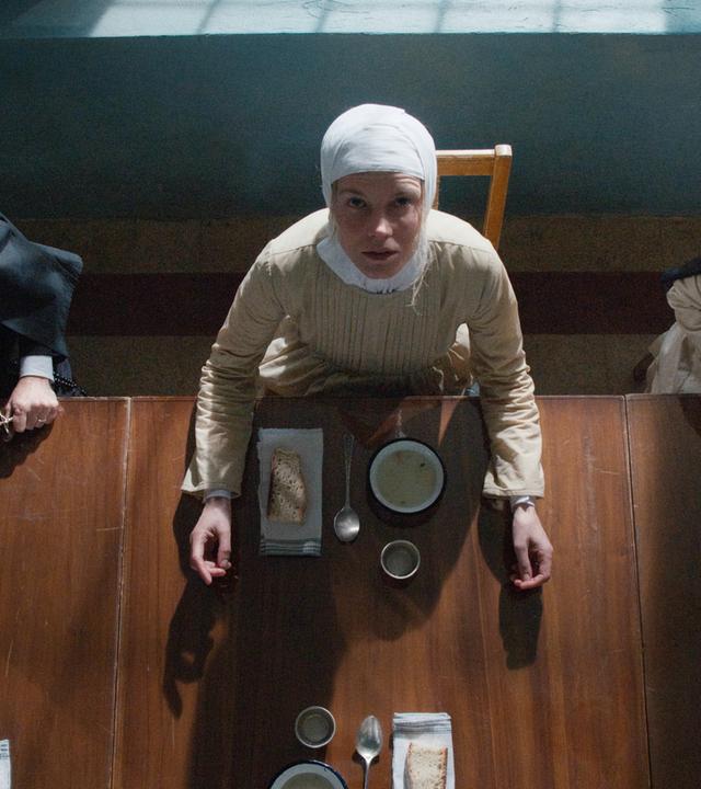 Blick von schräg oben auf drei Nonnen, die an einem Tisch sitzen und Teller vor sich haben.