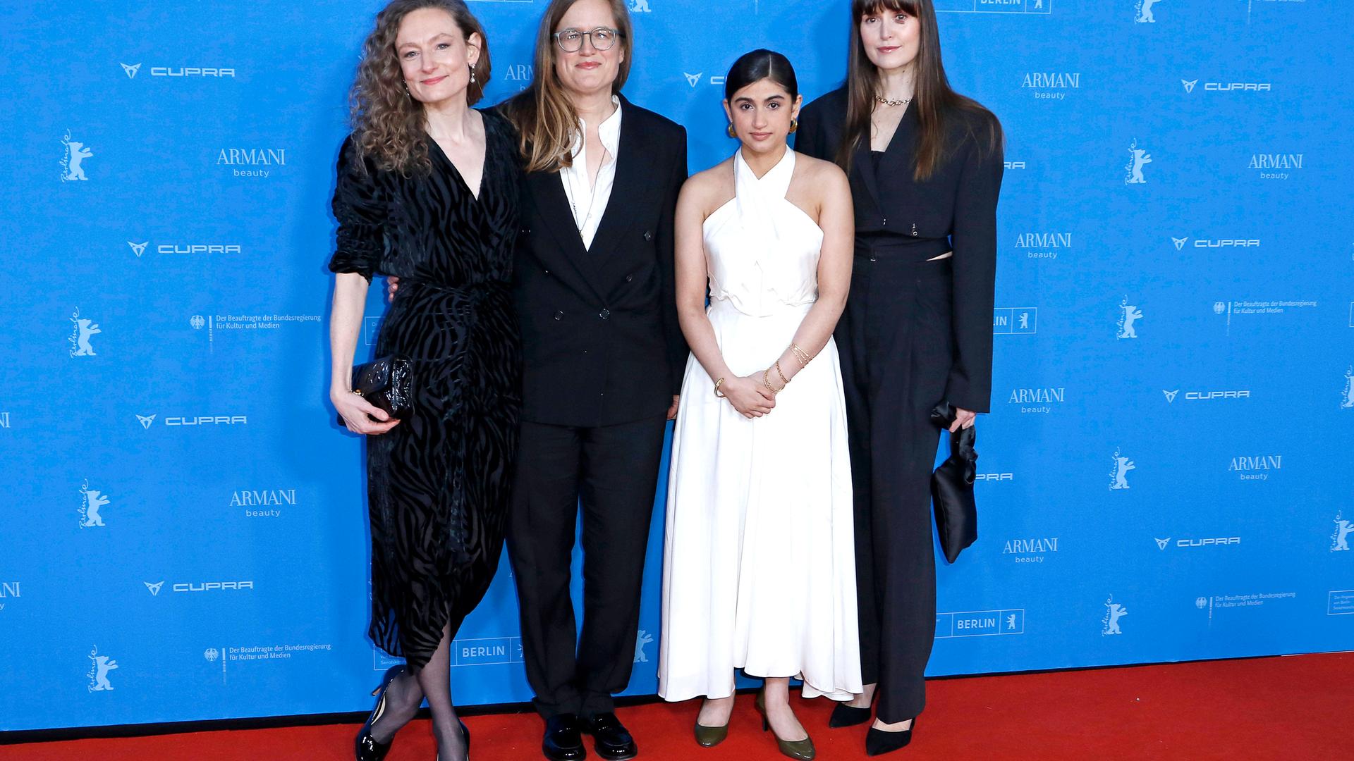 Vier Frauen stehen vor dem blauen Hintergrund der Berlinale-Pressekonferenz auf einem roten Teppich. Drei Frauen mittleren Alters tragen dunkle Anzüge und Kleider, eine jüngere Frau trägt ein schulterfreies weißes Kleid.