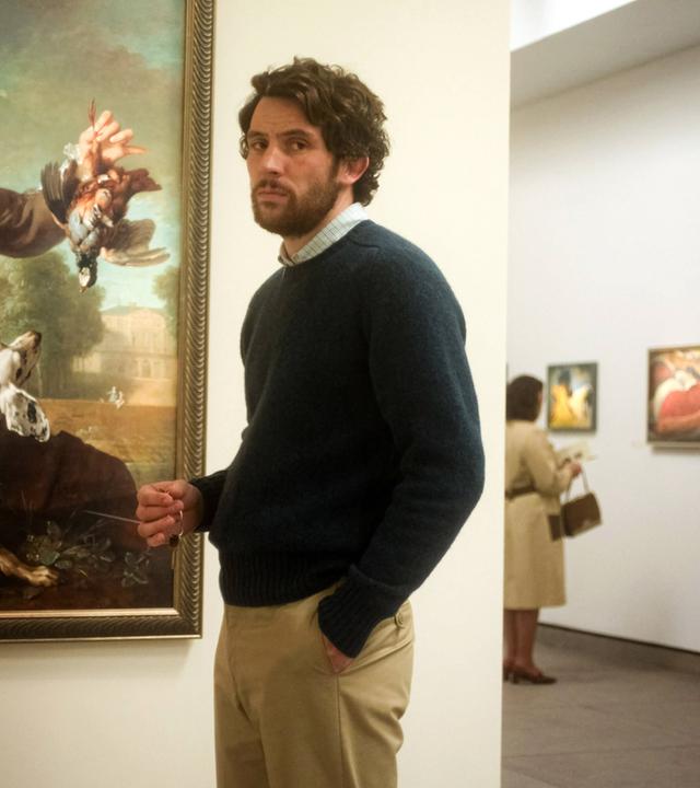 Ein Mann steht in einem Museum vor einem alten Ölgemälde, das einen Mann zeigt, der einen toten Vogel in der Hand hält und mit der anderen einen Hund hält.