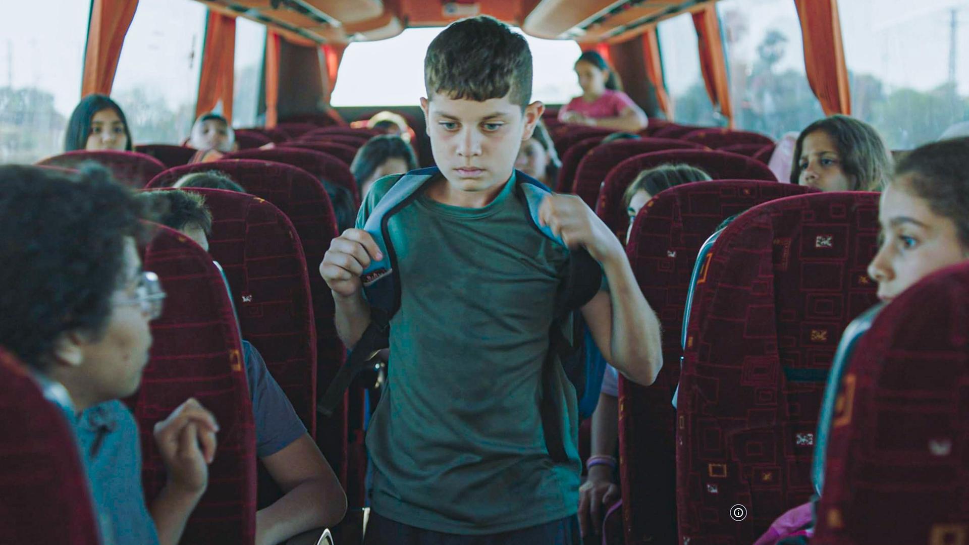 Ein junge mit Schulranzen auf dem Rücken geht durch den Gang zwischen den Sitzreihen in einem Bus.