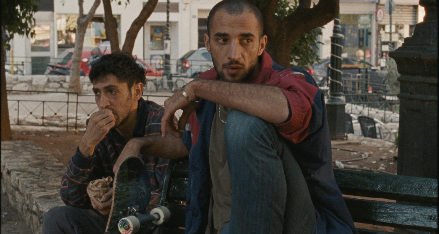 Zwei Männer sitzen unter Bäumen in einer Stadt.